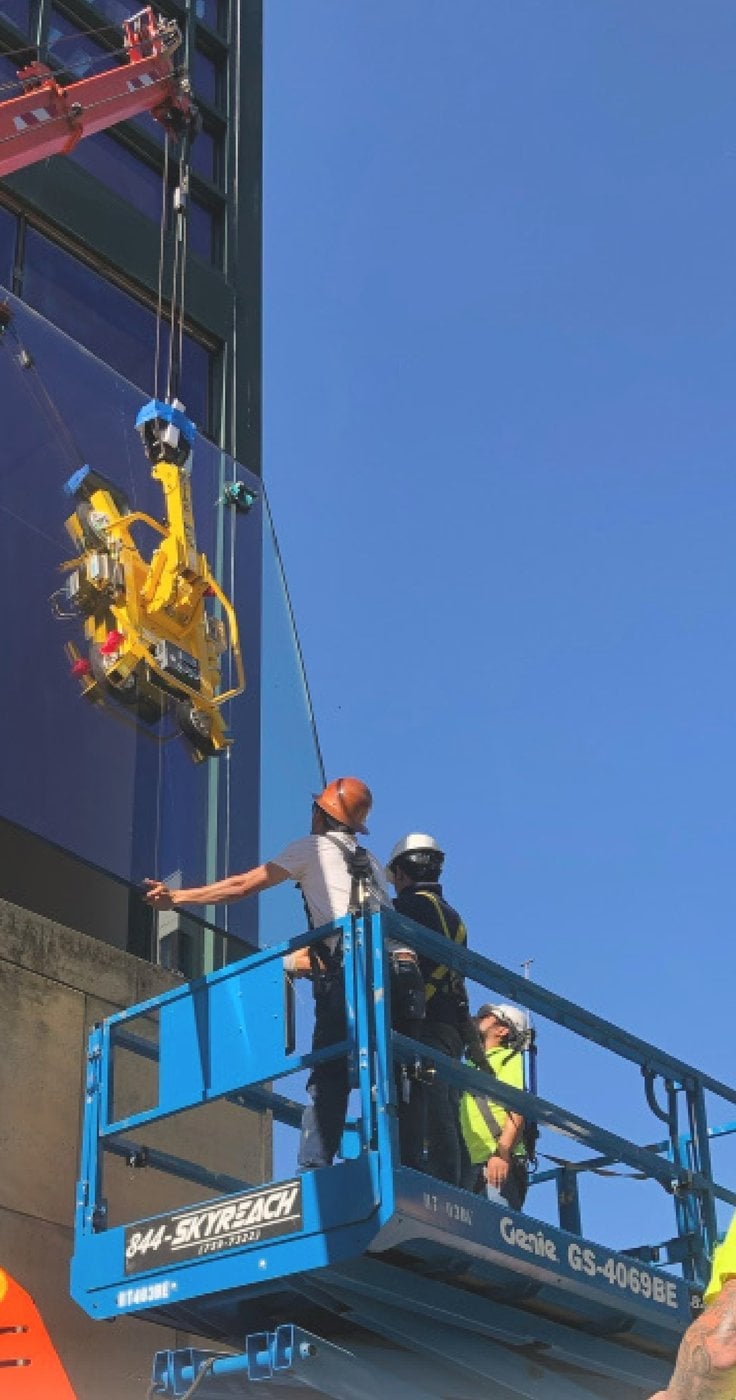 Skyreach crane-mounted glass manipulator setting a large glass panel on a building facade