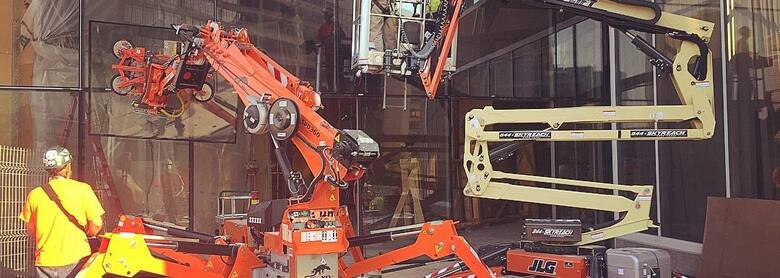 A Jekko mini crane and JLG boom lift working together on a Skyreach glass installation job site